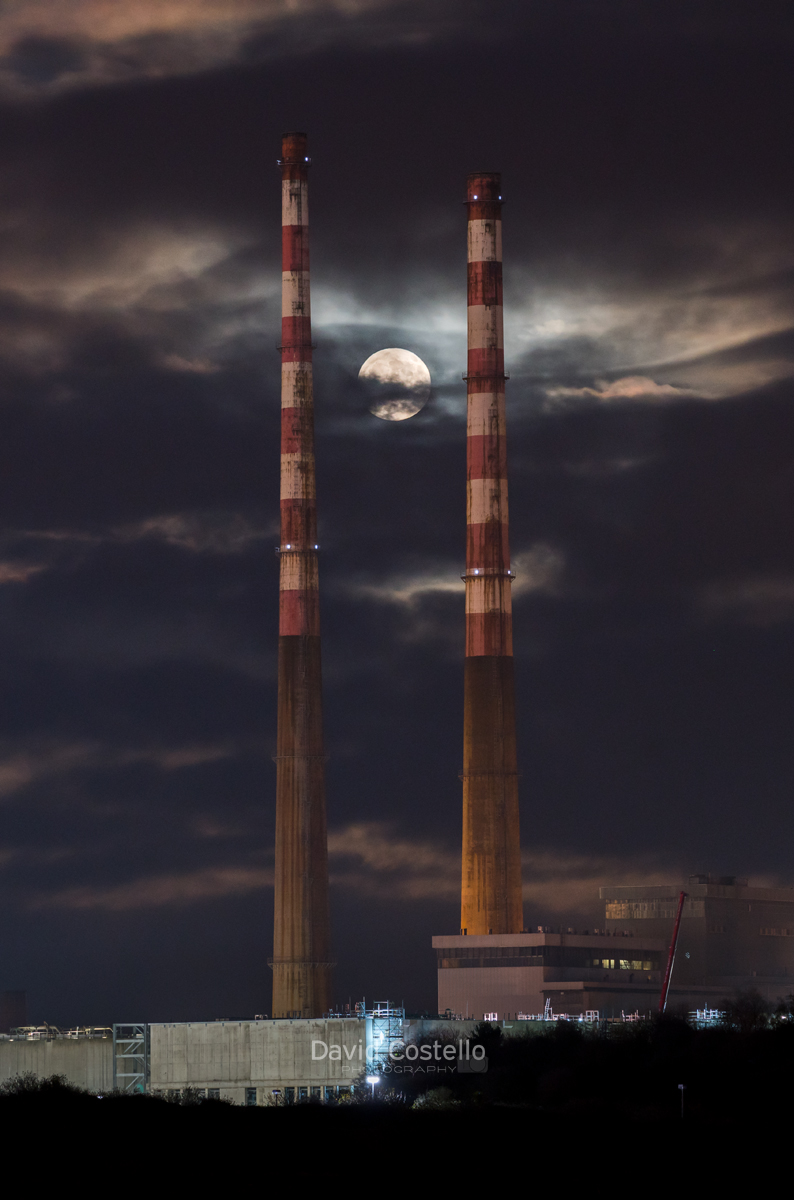 The full moon rising between the Poolbeg Chimneys in Dublin after breaking through the cloud.