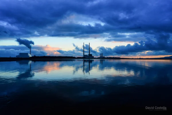 Poolbeg Chimneys reflecting in calm waters at blue hour.