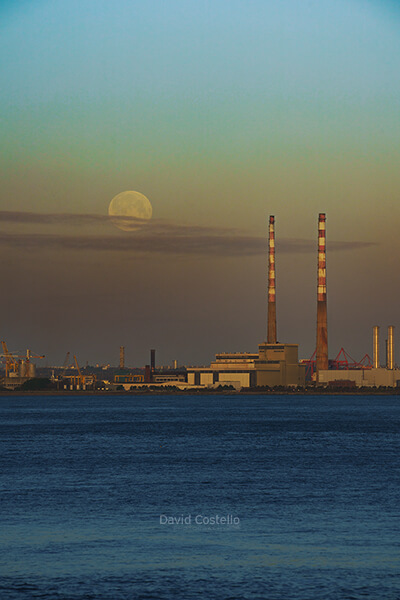 A crisp January morning as the full moon sets across Dublin bay beside the iconic Poolbeg Chimneys at sunrise.