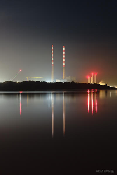 The repainted Poolbeg Chimneys reflect across Sandymount Strand on a misty night.