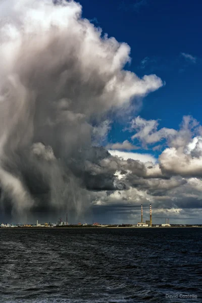 A heavy spring storm moves over one half of Dublin Bay with blue skies on the other side above the Poolbeg Chimneys.