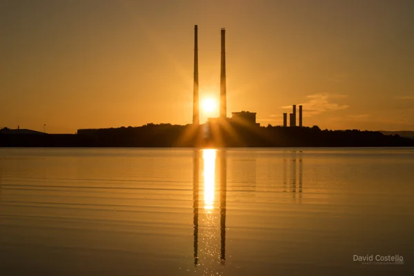 The sun rising between the Poolbeg Chimneys and reflections on the tide in Sandymount Beach.