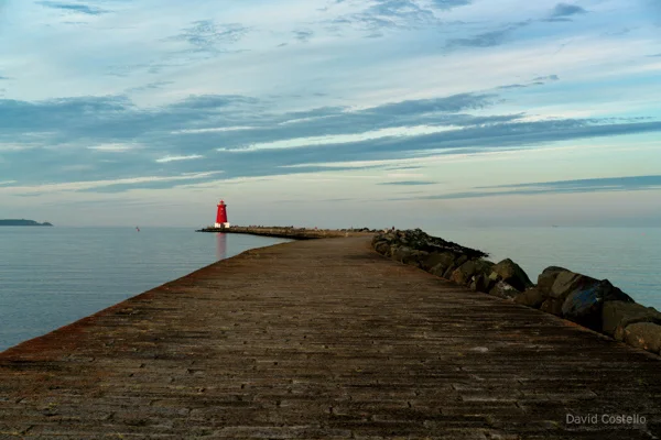Along The Great South Wall towards the Poolbeg Lighthouse which is reflecting in the water on a calm evening in Dublin.